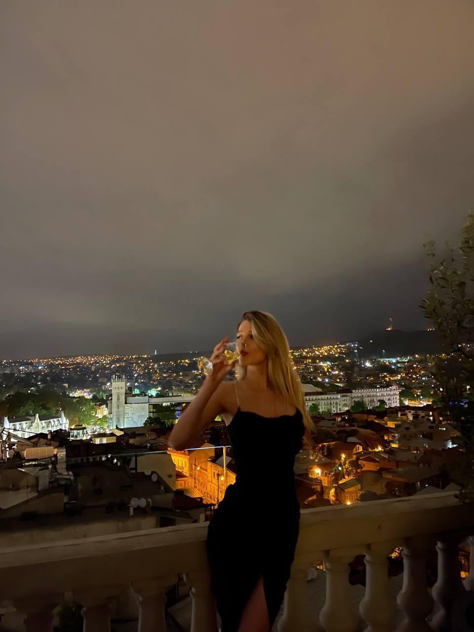 Ваймер с бокалом вина на фоне города.