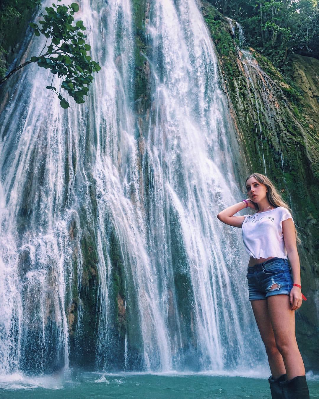 Прикольное фото на фоне водопада в коротких джинсовых шортах с голыми ногами.