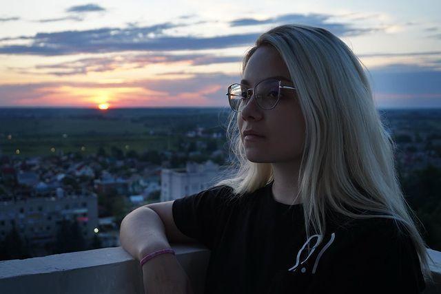 Красивое фото стримерши на крыше дома на фоне заката.