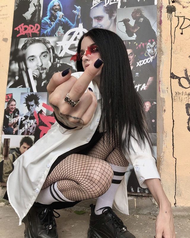 Крутая фотка vikanus в чулках в сеточку, показывающей фак на фоне рок плакатов.